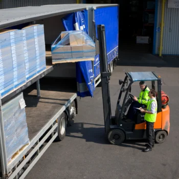 Forklift operator unloading pallets of carton board from a truck at HS Agency's logistics facility, showcasing efficient transportation and warehousing solutions for shipping and logistics across the U.K. and Ireland.