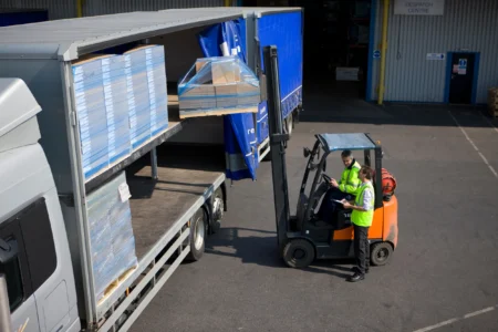 Forklift operator unloading pallets of carton board from a truck at HS Agency's logistics facility, showcasing efficient transportation and warehousing solutions for shipping and logistics across the U.K. and Ireland.