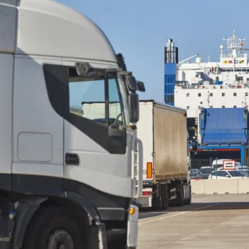 Trucks lined up at a port with a cargo ship in the background, representing HS Agency's logistics solutions for efficient transportation and warehousing services across the UK and Ireland.